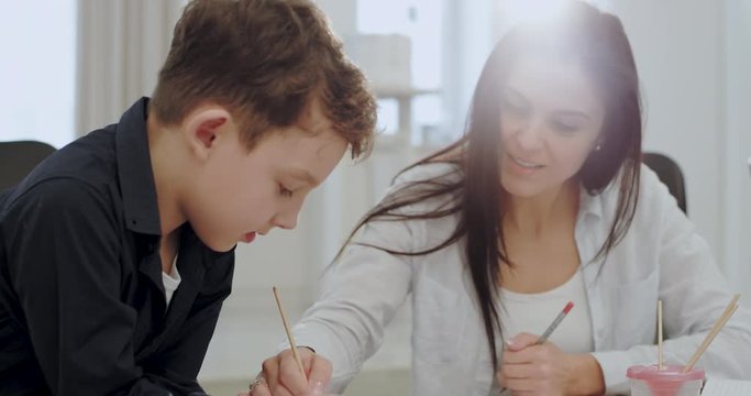 Portrait of a mature woman spending time with her son painting together for a school project , very attractive people in a modern house