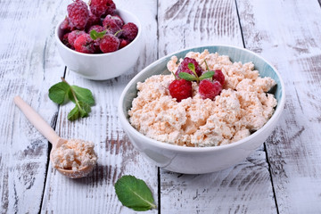 Cottage cheese topped with raspberries in a bowl on white wooden table
