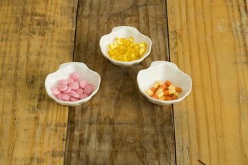 Drugs in the form of capsules, tablets and gelatin in oyster-shaped bowls on dirty wooden background