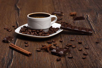 A cup with hot coffee and chocolate, cinnamon, star anise on a wooden table.
