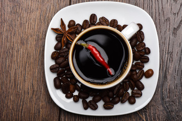Hot pepper pod in a cup with hot coffee. Coffee beans and star anise on a saucer.