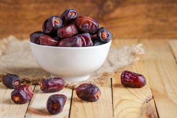 dates fruit  in white bowl and scattered on wooden table  