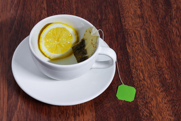 white cup with lemon slice and used tea bag saucer on wooden table copy space