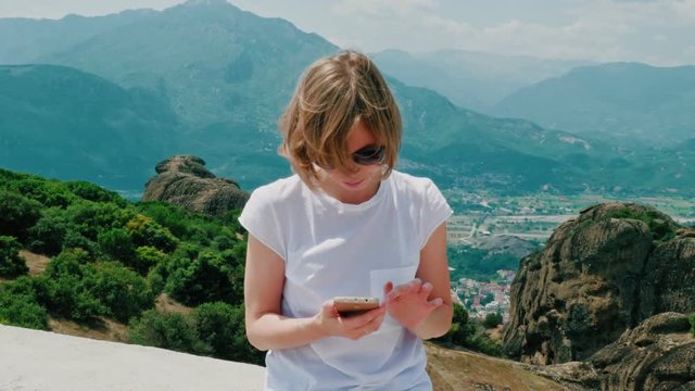 Young hipster girl wearing sunglasses using smartphone at amazing natural landscape with mountains