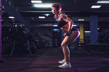 Fototapeta na wymiar Attractive fit sexy woman in the gym crouches with a barbell. Woman training back. Colored smoke