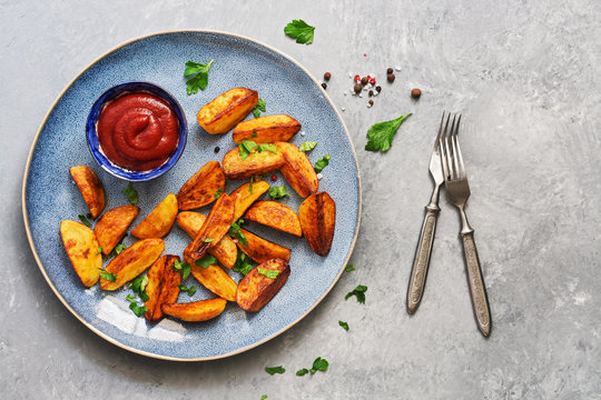 Fried potatoes with tomato sauce, spices and greens in a plate on a gray background. Overhead view, copy space.