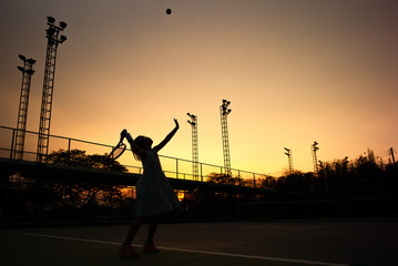 Silhouette portrait of Asian girl plays tennis at outdoor court with sunset sky in background