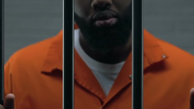 Dangerous African-American criminal holding prison bars, imprisonment, close-up