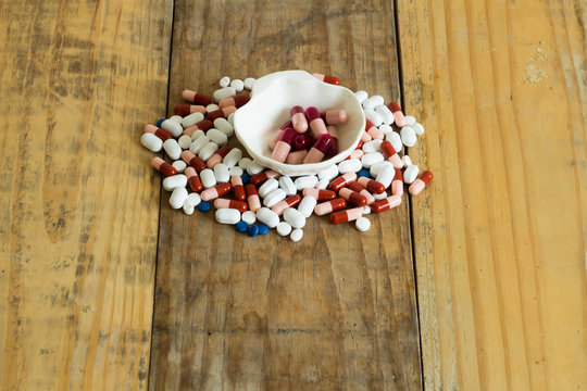 Drugs in the form of capsules, tablets and gelatin in oyster-shaped bowls on dirty wooden background