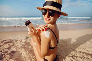 Woman applying sun cream on  tanned  shoulder. Skincare. Body Sun protection suncream. Bikini hat woman using moisturizing sunscreen lotion on back