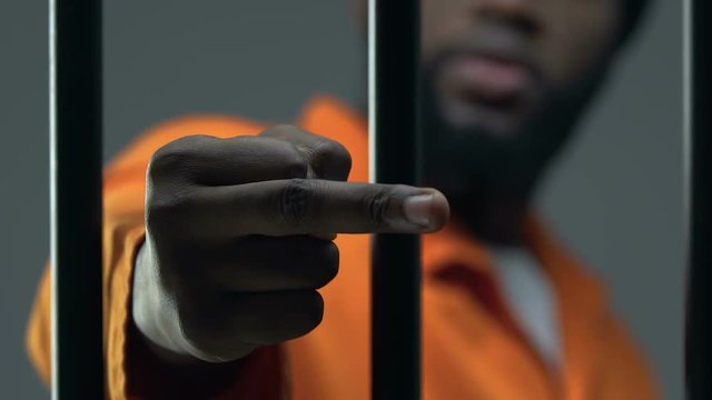 Angry Afro-American criminal showing middle finger through prison cell, conflict