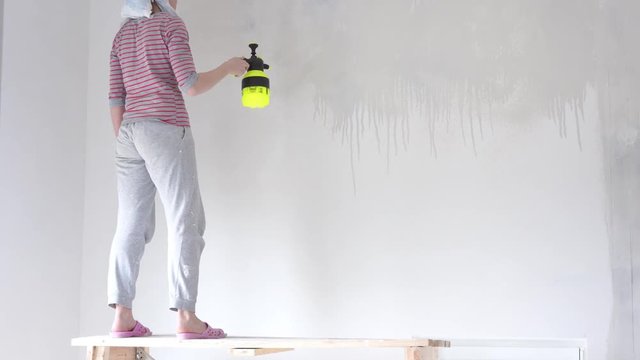 repair in the apartment - a young woman of European appearance makes repairs at home - wall priming