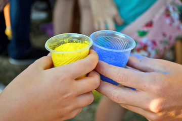 Two glasses with blue and yellow powder for holi war in the hands of two people