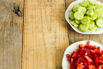 Sliced ​​cucumber and red pepper in plates on dirty wooden background