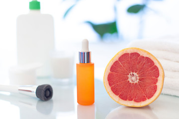 Vitamin C serum in the orange glass cosmetic bottle close up with a grapefruit in the bathroom