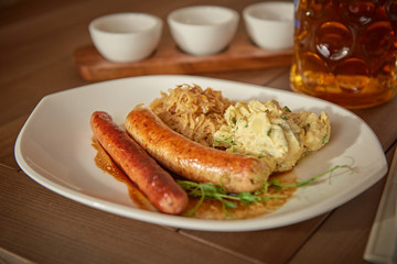 sausages with potatoes and sauerkraut with a beer on the table overlooking the lake
