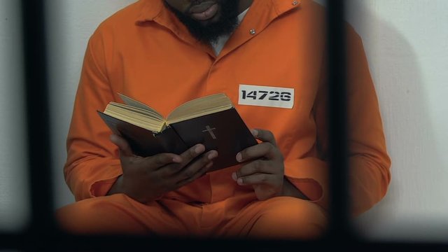 Black male prisoner reading holy bible in cell, hope for forgiveness, penance