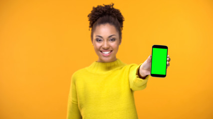 Happy female student showing smartphone with green screen, social network app