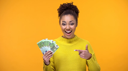 Happy black female pointing at euro banknotes in hand, financial success, salary