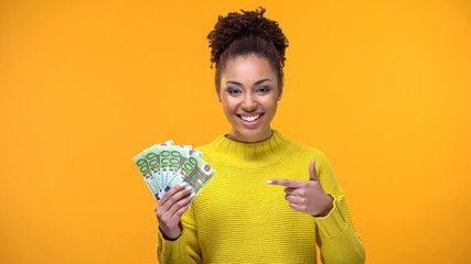 Cheerful young woman pointing at euro bills in hand, bank investment, cashback - obrazy, fototapety, plakaty