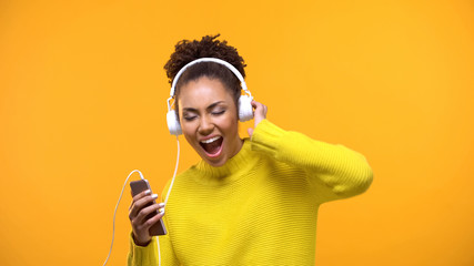 Pretty young woman in white headphones enjoying music sound on yellow background