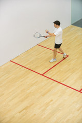 Squash player in action on squash court, side view/Young men playing match of squash