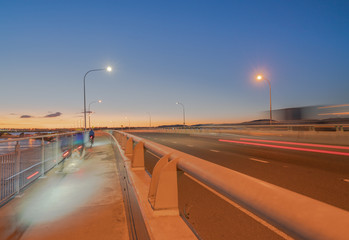 Fototapeta na wymiar Tauranga Harbour Bridge transport route with road and pedestrian and cycle path with glow of cyclists and vehicle passing lights