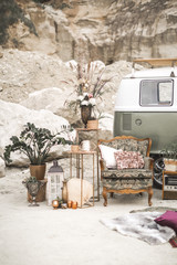 Grüner Hippie-Bus, Vintage-Sessel mit Kissen, Retro-Radio, goldene Metalldekorationen mit Pflanzen, Sukkulenten, Blumen und Kerzen, Pelzteppich auf dem Hintergrund der Wüstenlandschaft. Boho-Dekor © sofiko14