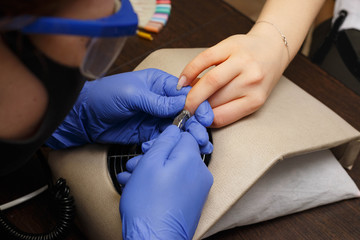 Closeup shot of a woman in a nail salon receiving a manicure by a beautician with electric nail file. Woman getting nail manicure. Beautician file nails to a customer