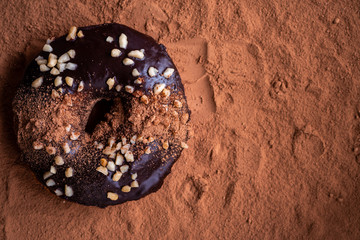 Donut in chocolate glaze and cocoa powder, top view. Dark background, copy space.