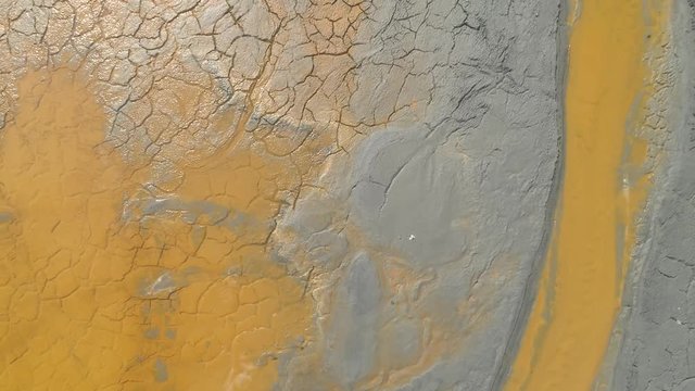 Cracked sludge with inserts of toxic yelow water at a mining disposal lake. Abstract toxic colored lake