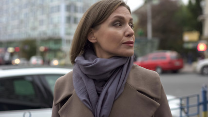 Worried woman standing on busy street, looking around waiting for appointment