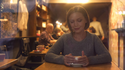 Attractive woman resting in cozy coffee-house enjoying hot flavored beverage