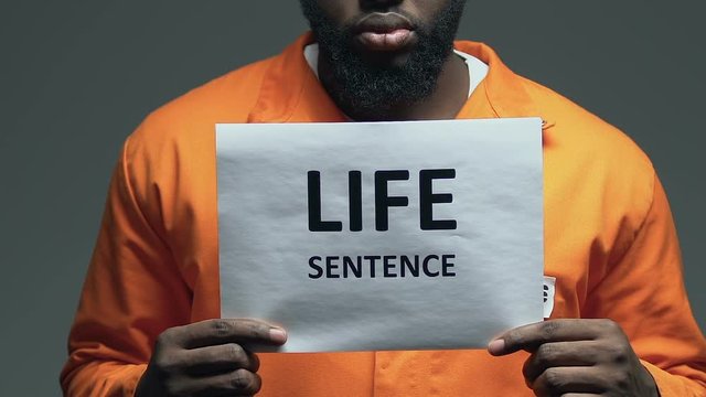 Life sentence phrase on cardboard in hands of Afro-American dangerous prisoner