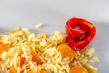 Cooked white rice with carrots and red fried sweet pepper on a white ceramic plate. Vegetarian food. Soft focus. Top view.