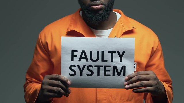Faulty system phrase on cardboard in hands of Afro-American prisoner, disorder