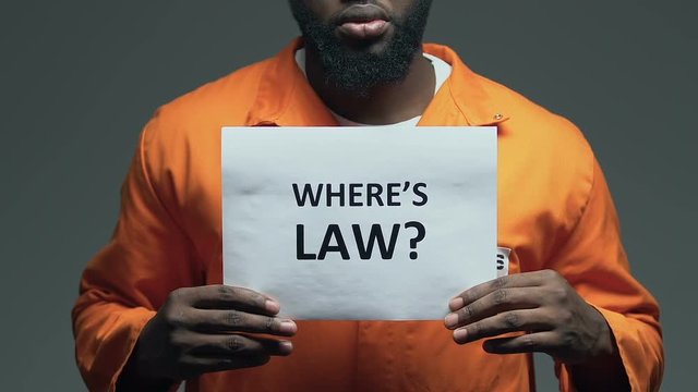 Wheres law question on cardboard in hands of Afro-American prisoner, disorder