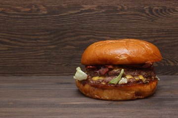 Fresh tasty homemade grilled burger with cheese and salad on wooden background with free space