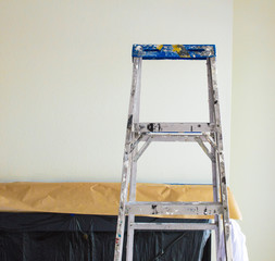 a paint spattered ladder in front of a fireplace covered with paper and plastic during painting