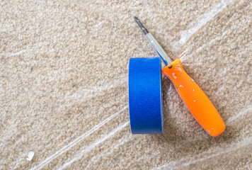blue painter's tape and orange screwdriver on a carpet covered with protective plastic