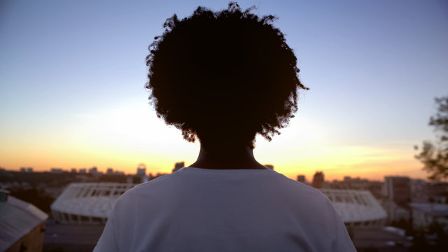 Afro-american curly haired woman enjoying sunset on roof, meditation, back view