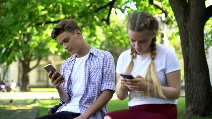 Indifferent teenagers scrolling smartphones in park, gadget addiction problem