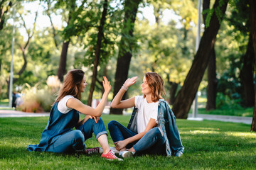 Happy female friends raising hands up giving high five in city park