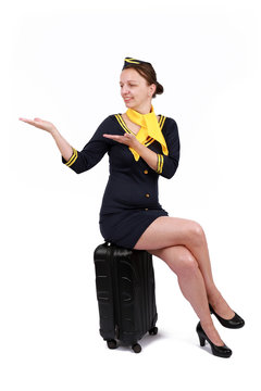 Stewardesse - Charming and smiling Stewardess Dressed In Blue Uniform sitting on her Suitcase . Isolated on white background