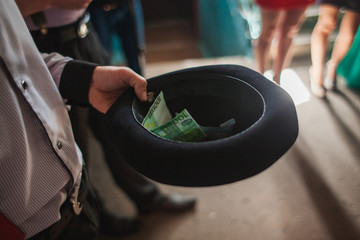 A man holds a black hat filled with euro money. Begging with a bowler hat. Euro money in black hat.