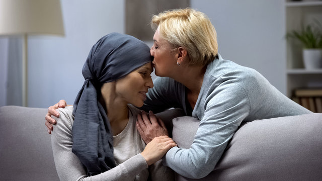 Mother hugging and kissing her hopeless daughter with cancer, family support