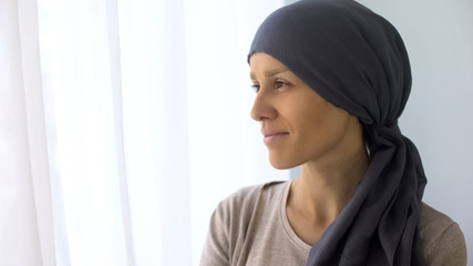 Happy woman in headscarf looking in window, recovery after cancer treatment