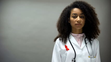 Afro-American female doctor with red ribbon, international AIDS awareness sign - Powered by Adobe