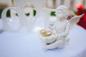 Wedding rings of the bride and groom are on a figurine in the form of small angel.