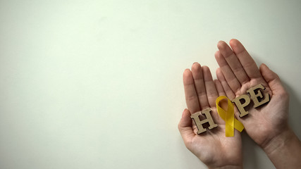 Yellow ribbon and hope word in hands, childhood cancer awareness, healthcare